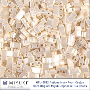 May include: Close-up of a pile of HTL-0592 Antique Ivory Pearl Ceylon Tila beads. The beads are rectangular with two holes and have a pearlescent finish. The beads are 100% Original Miyuki Japanese Tila Beads.