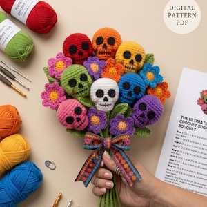 Puede incluir: Un ramo de ganchillo con calaveras y flores multicolores en rojo, naranja, amarillo, verde, azul, rosa y morado. Los tallos están atados con una cinta estampada. Junto al ramo hay ovillos de lana, ganchillos y un patrón en PDF.