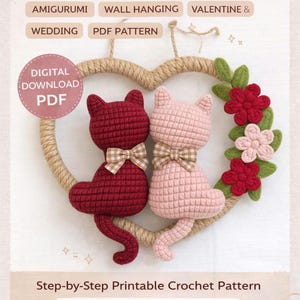 Può includere: Una ghirlanda a uncinetto a forma di coppia di gatti con una cornice a forma di cuore. La ghirlanda presenta due gatti amigurumi, uno bordeaux e uno rosa, ciascuno con un papillon. La ghirlanda è decorata con fiori rossi e rosa e foglie verdi. Il testo "Crochet Cat Couple Wreath" è in alto.