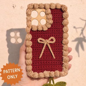 May include: A handmade crochet phone cover in a deep red color, with a beige border and a bow detail. The cover features a cherry design at the bottom. Text on the image reads "Crochet Phone Cover" and "PDF Crochet Pattern".
