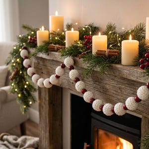 May include: A decorative garland featuring alternating white crocheted spheres and smaller dark red wooden beads, draped across a rustic wooden mantelpiece adorned with green pine branches, cinnamon sticks, red berries, and lit pillar candles.