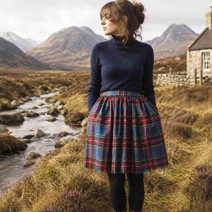 May include: A dark blue long-sleeved turtleneck sweater paired with a knee-length pleated skirt featuring a blue, red, and green plaid tartan pattern. The skirt has a gathered waistline and a full silhouette, worn over solid black leggings.