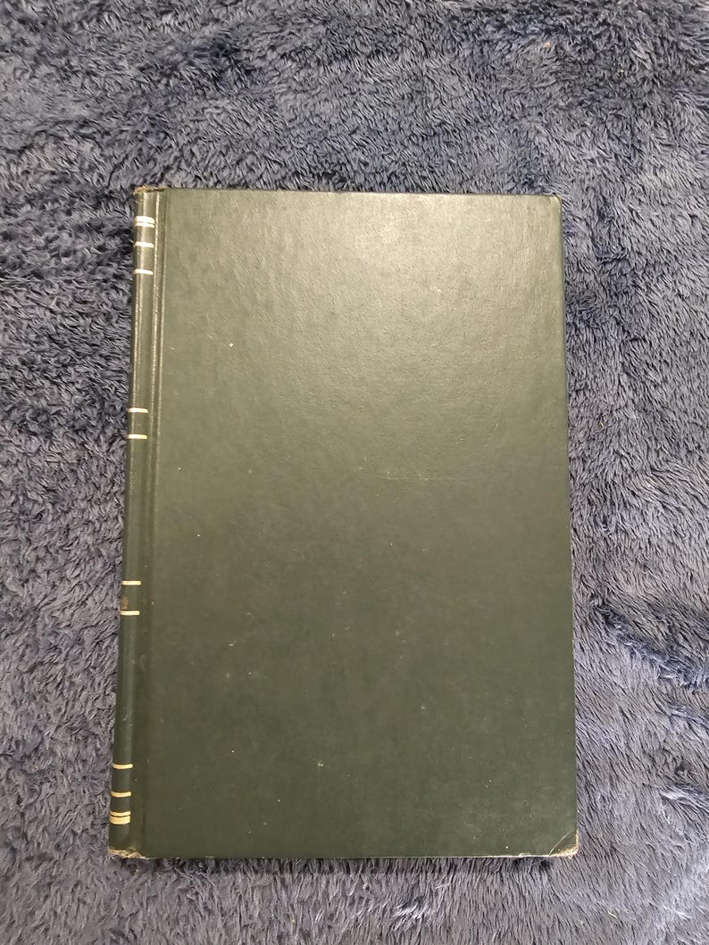 May include: A hardcover book with a dark green cover. The spine is visible with gold accents. The book is rectangular and appears to be in good condition. The background is a textured, dark blue surface.