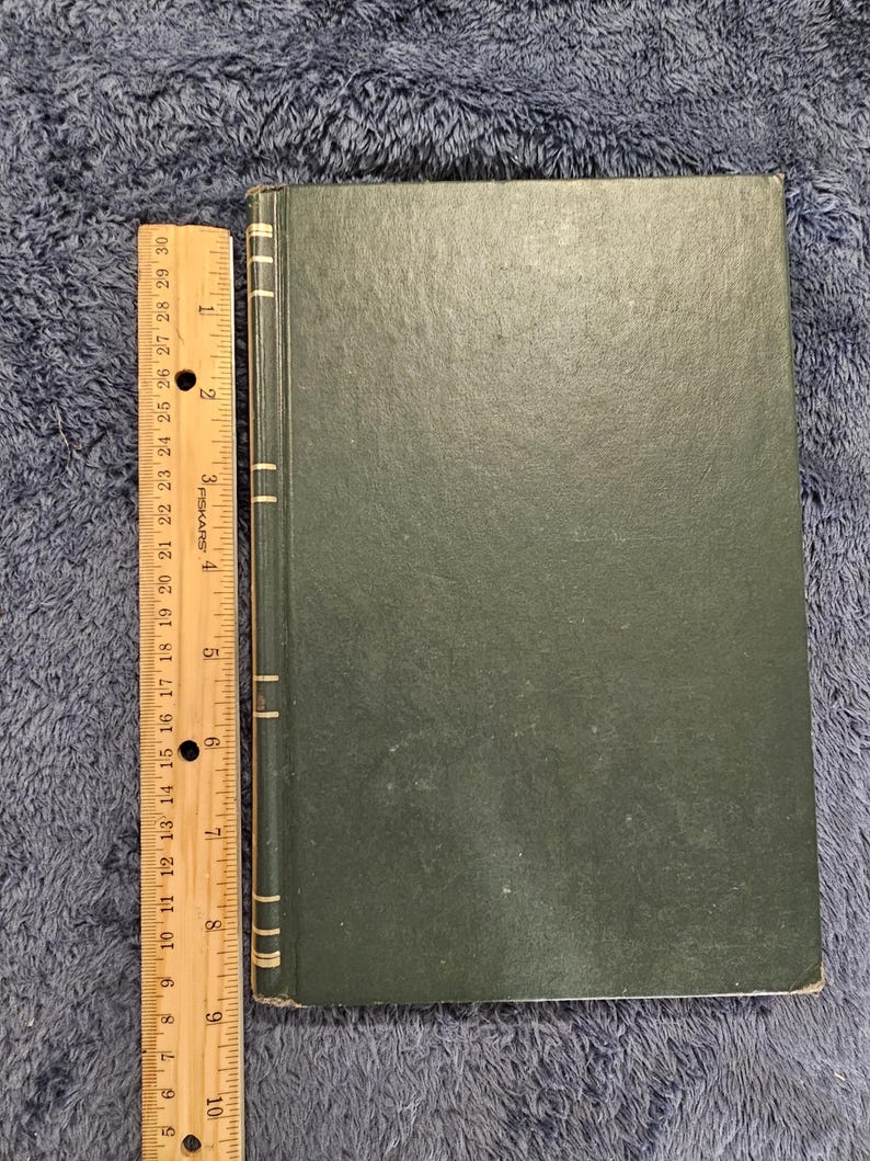 May include: A dark green book with a ruler alongside it. The book has a textured cover and a spine with vertical lines. The ruler is marked in inches, showing measurements up to 30 inches.