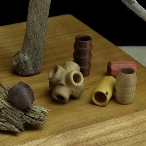 Könnte beinhalten: Eine Sammlung kleiner, handgefertigter Holzperlen und Komponenten in verschiedenen natürlichen Holztönen, darunter ein multidirektionales Verbindungsstück, zylindrische Formen mit gerillten Texturen und glatte, abgerundete Formen.