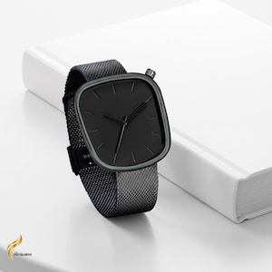 Puede incluir: Un reloj de pulsera negro con una esfera cuadrada y una correa de malla. El reloj tiene un diseño minimalista con manecillas y marcadores negros. La correa es de color gris oscuro. El reloj se muestra sobre una superficie blanca.