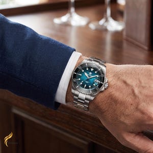 May include: A stainless steel wristwatch with a metallic teal blue dial, a black rotating bezel with white numerals, and a date window at the three o'clock position. The watch features a silver-toned link bracelet and a round case design.