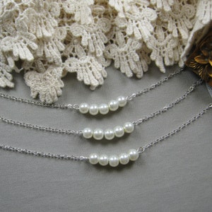 Puede incluir: Tres cadenas de plata con detalles de perlas blancas. Cada cadena tiene una fila de perlas en forma de curva.