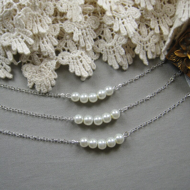 Puede incluir: Tres cadenas de plata con detalles de perlas blancas. Cada cadena tiene una fila de perlas en forma de curva.