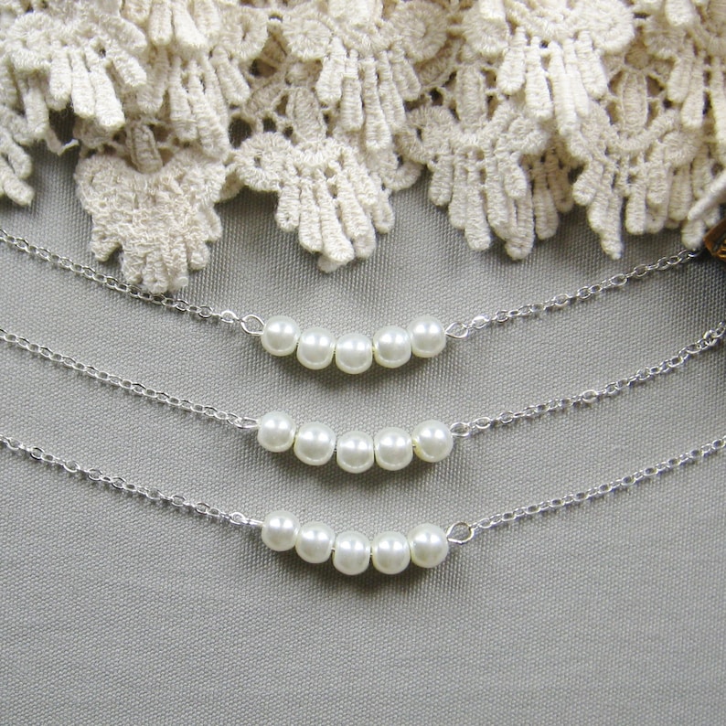 Puede incluir: Tres collares de plata con una fila de perlas blancas en cada uno. Los collares est&aacute;n superpuestos.