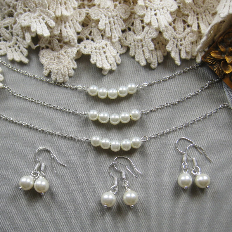 Puede incluir: Tres collares de cadena plateada con hileras de perlas blancas y un par de pendientes plateados con gotas de perlas blancas.