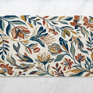 Pode incluir: Tapete retangular com um design floral e de peixes. O tapete apresenta um fundo creme com motivos florais e de peixes azuis, laranja e amarelos. O tapete é colocado sobre um chão de mármore branco.
