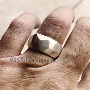 May include: A silver ring with a faceted design. The ring is wide and has a geometric pattern. The ring is on a finger. The text "925SilverVinaya" is visible.