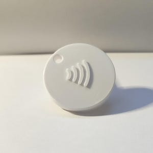 May include: A small, circular white plastic tag featuring a raised wireless signal icon embossed on the front surface. The tag includes a single circular hole near the top edge, designed for attachment to a keychain or other personal items.