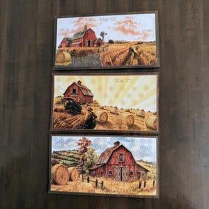 Op de afbeelding: Drie rechthoekige spelkaarten met boerderijtaferelen, rode schuren, hooibalen en velden. Elke kaart bevat cirkelvormige scoremarkeringen en de tekst Totaal 100, Totaal 125 en Totaal 60, met illustraties van een windmolen en een tractor.