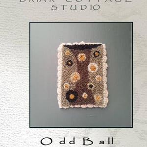 Puede incluir: Patrón de diseño de aguja de punzón o de bordado para un proyecto de tejido de alfombras llamado "Odd Ball". El diseño presenta una alfombra marrón y beige con un borde rosa y una variedad de círculos coloridos.