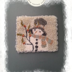 May include: A small, white, winter-themed needlepoint project featuring a snowman with a black hat and scarf. The background is a light beige with a brown branch and red berries. The text "Winter White Mini" is printed below the image.