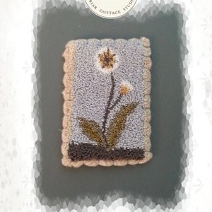 Puede incluir: Una pequeña alfombra azul claro y marrón con un diseño de flor blanca. La alfombra está enmarcada con un borde de color crema. La alfombra está etiquetada como "DANDY MINI" y es un producto de "BRIAR COTTAGE STUDIO".