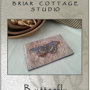 Peut inclure: Un motif de point d'aiguille ou de broderie pour un papillon. Le motif est sur un fond rose avec un papillon dans des tons de bleu, vert, orange et marron. Le motif mesure 21 cm sur 15 cm. Le motif s'appelle "Butterfly" et est de Briar Cottage Studio.