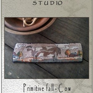 May include: A rectangular punch needle design featuring a cow in a fall landscape. The design is approximately 10.5 inches long and 3 inches wide. The text "Primitive fall-Cow" is displayed below the design. The image also includes the text "Briar Cottage Studio".