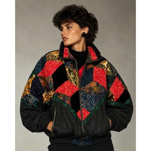 May include: A quilted bomber jacket featuring a patchwork design of red, black, and multi-colored fabric panels with gold-toned swirling embroidery. The jacket includes a high collar, a full-length front zipper, and black ribbed cuffs and hem.