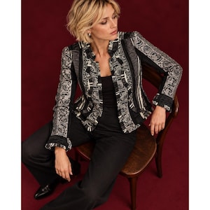 May include: A black and white patterned jacket featuring a paisley print, vertical striped panels, and ruffled trim along the front opening. The jacket is worn over a solid black top and paired with black trousers and black leather shoes.