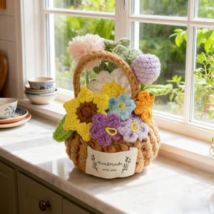 Puede incluir: Una cesta de ganchillo hecha a mano llena de flores coloridas, incluyendo girasoles, margaritas y otras flores en tonos de amarillo, morado, azul y naranja. La cesta tiene un asa y una etiqueta que dice "Handmade with love."