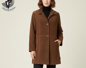 May include: A brown suede coat with a button-up front, collared neckline, and two front pockets. The coat is knee-length and has long sleeves. The model is wearing a black turtleneck and black trousers.