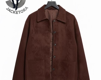 May include: A brown jacket with a collared neckline and two large front pockets. The jacket has a button-up closure and is hanging on a black hanger. The word "JACKETORA" is visible in the upper left corner.