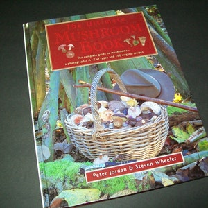 May include: The Ultimate Mushroom Book cover features a basket full of mushrooms, a hat, and a walking stick. The book title is in red with white lettering. The book's authors are Peter Jordan and Steven Wheeler.