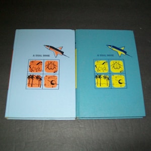May include: Two blue book covers with a rocket ship illustration and the text "A REAL BOOK" on each. The book covers have a yellow and orange design with illustrations of a horse, a bug, palm trees, a star, and a crescent moon.