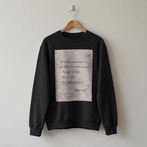Op de afbeelding: Zwarte sweatshirt met een bedrukt ontwerp. Het ontwerp bevat handgeschreven tekst op een achtergrond van gelijnd papier. De tekst luidt: "We chase misprinted lies, We face the path of time, And yet I fight, Yet I fight, This battle all alone. Layne Staley."