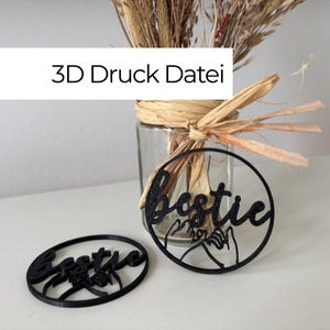 Op de afbeelding: Twee zwarte ronde 3D-geprinte ornamenten met het woord bestie in cursief schrift boven een afbeelding van twee handen die een pinkbelofte doen. De tekst 3D Druck Datei is zichtbaar in het bovenste gedeelte boven een glazen pot.