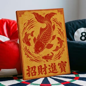 Könnte beinhalten: Ein rechteckiger Leinwanddruck mit goldgelbem Hintergrund und einer roten Illustration von vier Koi-Fischen, die im Kreis schwimmen. Am unteren Rand des Drucks befinden sich die roten chinesischen Schriftzeichen 招財進寶, umrahmt von einer Bordüre.