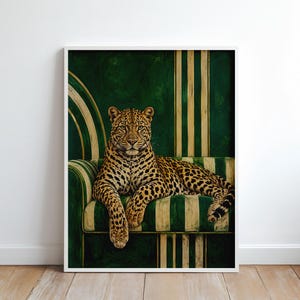 Pode incluir: Uma impressão de arte de parede emoldurada apresentando um leopardo descansando em um sofá listrado de verde e creme. O leopardo tem uma pelagem manchada e está posicionado centralmente. O fundo consiste em listras verticais verdes e creme.