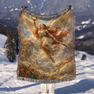 May include: A woven throw blanket featuring a classical painting of a winged figure holding a laurel wreath and a sword. The artwork depicts a woman in flowing robes, set against a backdrop of clouds, buildings, and figures. The blanket has a fringed edge.