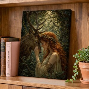May include: A framed wall art print depicting a person with long red hair and a floral crown gently touching the forehead of a large brown stag. The scene is set within a dense, dark green forest with dappled sunlight filtering through the trees.