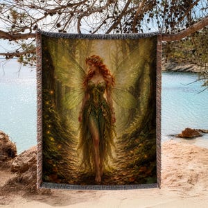 May include: A woven throw blanket featuring a detailed illustration of a red-haired fairy with large translucent wings, wearing a green leaf-inspired dress, standing on a forest path surrounded by tall trees and glowing golden light particles.