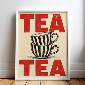 May include: A framed wall art print featuring a cream-colored background with the word TEA in large, textured red block letters at the top and bottom. In the center, two black and white striped teacups are stacked vertically on top of each other.