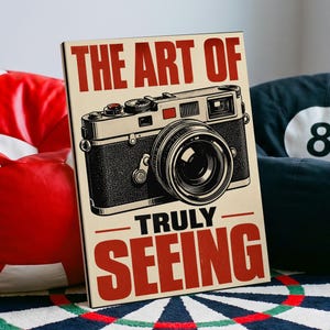 Könnte beinhalten: Ein rechteckiger Wandkunstdruck mit einer schwarz-weißen Illustration einer Kamera im Vintage-Stil. Der Text THE ART OF ist in Rot über der Kamera gedruckt, und die Wörter TRULY SEEING stehen in Rot unter der Kamera auf einem cremefarbenen Hintergrund.