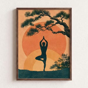Könnte beinhalten: Ein gerahmter Kunstdruck mit der dunklen Silhouette einer Person in der Baum-Yoga-Pose. Der Hintergrund zeigt eine große orangefarbene Sonne und eine kleinere gelbe Sonne, mit einem dunkelgrünen Kiefernzweig darüber und einem dunkelgrünen Boden.