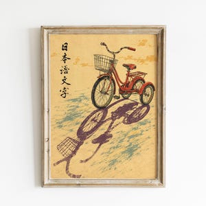 Könnte beinhalten: Ein gerahmter Kunstdruck, der ein rotes Dreirad mit einem Frontkorb auf gelbem Hintergrund zeigt. Die Illustration enthält japanische Schriftzeichen auf der linken Seite und stellt das Fahrrad mit einem langen, violetten Schatten dar.