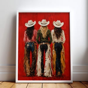 Könnte beinhalten: Ein gerahmter Wandkunstdruck, der drei Figuren von hinten zeigt, die jeweils einen weißen Cowboyhut, ein langärmeliges Hemd, eine dunkelblaue Jeans und Lederchaps mit Fransen tragen, vor einem strukturierten, leuchtend roten Hintergrund.