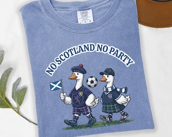Puede incluir: Una camiseta azul bígaro con un gráfico de dos gansos vestidos con atuendo escocés, uno de ellos sosteniendo una bandera escocesa, con un balón de fútbol y el texto NO SCOTLAND NO PARTY impreso en blanco sobre los gansos en la parte frontal.