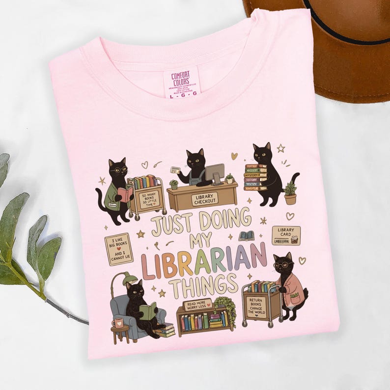 Comfort Colors Blossom black cat librarian shirt featuring cute black cats reading books, library checkout desk, book cart, stacked books, library card, cozy reading chair, funny library illustrations, school librarian tee for library staff, reading teacher, book lover and BookTok fans.