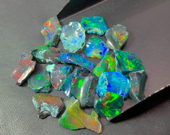 May include: A collection of raw, unpolished opal gemstones featuring vibrant flashes of blue, green, and red color play. The stones are irregular in shape and texture, displaying a dark, translucent base with intense iridescent light reflections.