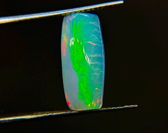 以下が含まれることがあります： 鮮やかな緑と青色の模様が特徴的な長方形のオパール宝石。 オパールは黒い背景に対してピンセットで保持されています。 宝石は研磨された表面を持ち、赤と黄色の閃光を示しています。