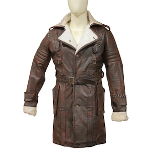 May include: A brown leather coat with a white shearling collar and lining. The coat features a belted waist, multiple pockets, and decorative straps with buckles. The sleeves have shearling cuffs and stitched detailing. The coat is displayed on a mannequin.