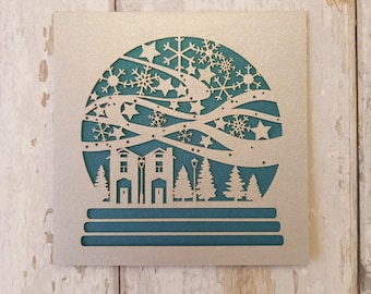 Tarjeta navideña de bola de nieve cortada a láser: diseño hecho a mano en plata y verde azulado.