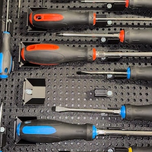 Może przedstawiać: Kolekcja śrubokrętów z czarnymi uchwytami i kolorowymi akcentami, w tym czerwonym, zielonym, niebieskim i żółtym. Narzędzia są uporządkowane w czarnej wkładce z pianki, prezentując różne rozmiary i typy głowic. Obraz podkreśla różnorodność narzędzi.